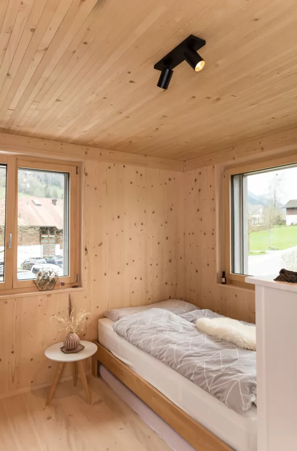 Truberholz Mehrfamilienhaus. Aussenschalung vor vergrautes Falzbrett aus Tanne, integrierte Sauna in Ferienwohnung, Saunawand aus Tanne, Möbel in der Saune aus Arven Holz, Truberholz-Wände innen sichtbar, inklusive Decke Dachschräge, Gebäudehülle Truberholz sichtbar, Innendecke Brettstapel, Boden ist alles Trockenbauaufbau, Zimmer und Bad aus Tannen Holz und allgemein Räume sind Buchenriemenboden. Türen sind alle Massivholz mit Blockfutter aus Tanne.