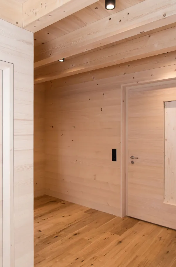 Innenansicht eines modernen Holzbaus mit sichtbaren Balken, natürlichen Holzoberflächen und massgefertigten Einbauten. Grosszügige Fensterflächen sorgen für viel Tageslicht und unterstreichen die warme, ruhige Wohnatmosphäre. Hochwertige Materialien und präzise Schreinerarbeiten prägen das Gesamtbild.