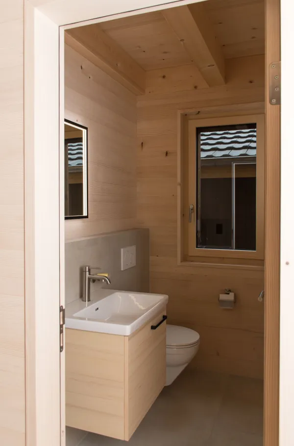 Innenansicht eines modernen Holzbaus mit sichtbaren Balken, natürlichen Holzoberflächen und massgefertigten Einbauten. Grosszügige Fensterflächen sorgen für viel Tageslicht und unterstreichen die warme, ruhige Wohnatmosphäre. Hochwertige Materialien und präzise Schreinerarbeiten prägen das Gesamtbild.