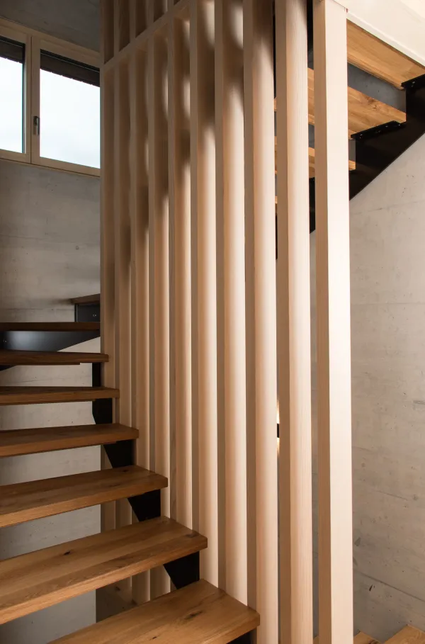 Innenansicht eines modernen Holzbaus mit sichtbaren Balken, natürlichen Holzoberflächen und massgefertigten Einbauten. Grosszügige Fensterflächen sorgen für viel Tageslicht und unterstreichen die warme, ruhige Wohnatmosphäre. Hochwertige Materialien und präzise Schreinerarbeiten prägen das Gesamtbild.