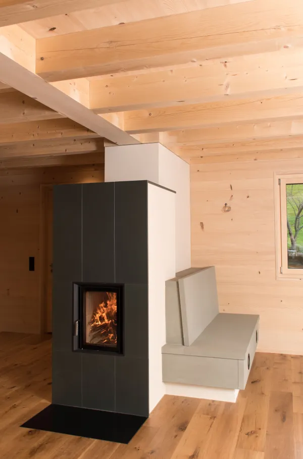 Innenansicht eines modernen Holzbaus mit sichtbaren Balken, natürlichen Holzoberflächen und massgefertigten Einbauten. Grosszügige Fensterflächen sorgen für viel Tageslicht und unterstreichen die warme, ruhige Wohnatmosphäre. Hochwertige Materialien und präzise Schreinerarbeiten prägen das Gesamtbild.