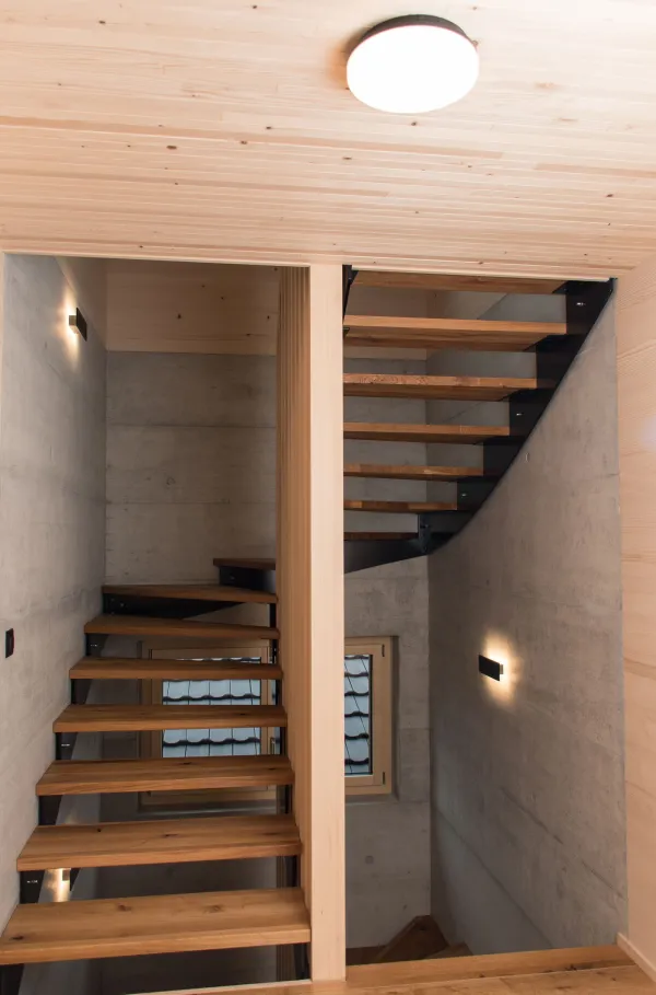 Innenansicht eines modernen Holzbaus mit sichtbaren Balken, natürlichen Holzoberflächen und massgefertigten Einbauten. Grosszügige Fensterflächen sorgen für viel Tageslicht und unterstreichen die warme, ruhige Wohnatmosphäre. Hochwertige Materialien und präzise Schreinerarbeiten prägen das Gesamtbild.