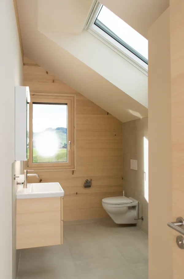 Innenansicht eines modernen Holzbaus mit sichtbaren Balken, natürlichen Holzoberflächen und massgefertigten Einbauten. Grosszügige Fensterflächen sorgen für viel Tageslicht und unterstreichen die warme, ruhige Wohnatmosphäre. Hochwertige Materialien und präzise Schreinerarbeiten prägen das Gesamtbild.