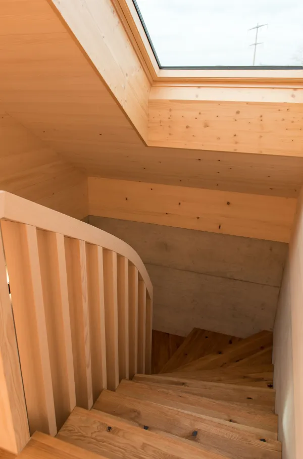 Innenansicht eines modernen Holzbaus mit sichtbaren Balken, natürlichen Holzoberflächen und massgefertigten Einbauten. Grosszügige Fensterflächen sorgen für viel Tageslicht und unterstreichen die warme, ruhige Wohnatmosphäre. Hochwertige Materialien und präzise Schreinerarbeiten prägen das Gesamtbild.