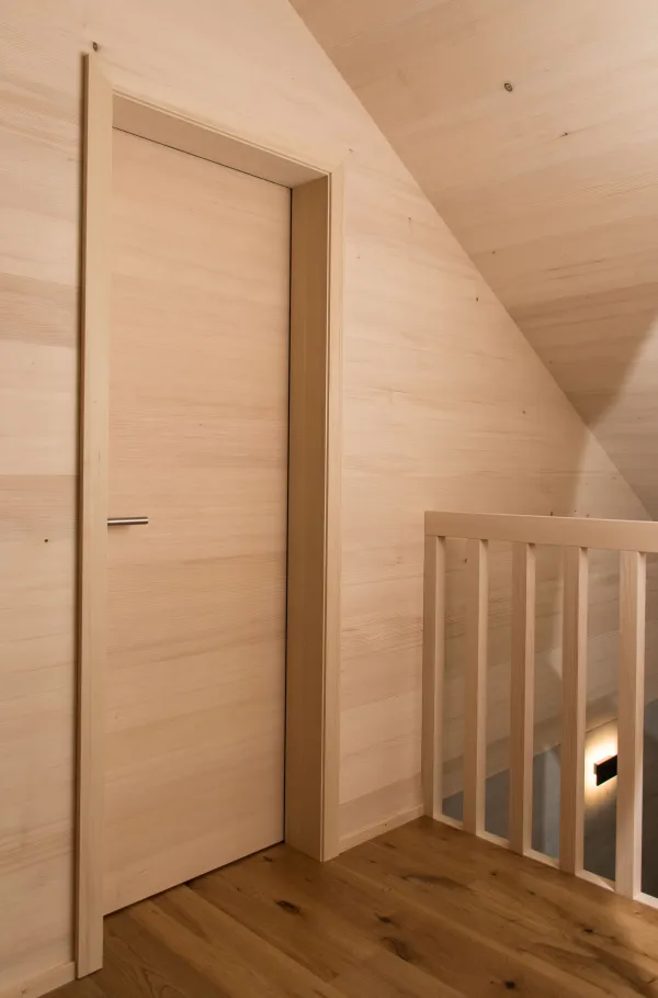 Innenansicht eines modernen Holzbaus mit sichtbaren Balken, natürlichen Holzoberflächen und massgefertigten Einbauten. Grosszügige Fensterflächen sorgen für viel Tageslicht und unterstreichen die warme, ruhige Wohnatmosphäre. Hochwertige Materialien und präzise Schreinerarbeiten prägen das Gesamtbild.