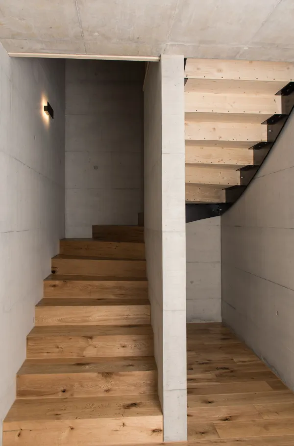 Innenansicht eines modernen Holzbaus mit sichtbaren Balken, natürlichen Holzoberflächen und massgefertigten Einbauten. Grosszügige Fensterflächen sorgen für viel Tageslicht und unterstreichen die warme, ruhige Wohnatmosphäre. Hochwertige Materialien und präzise Schreinerarbeiten prägen das Gesamtbild.