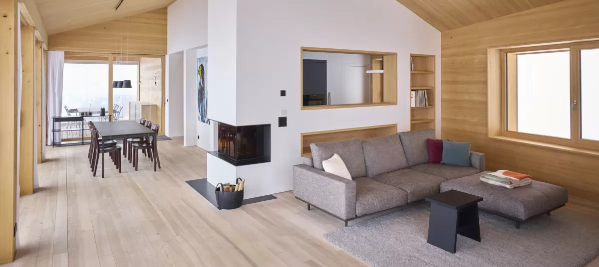 Wohnbereich Ferienwohnung im Luzern mit integriertem Cheminé und Liegesofa vor der Glasfron. Truberholzwände sind ersichtlich. Raumhöhe ist offen bis unter die Firts.