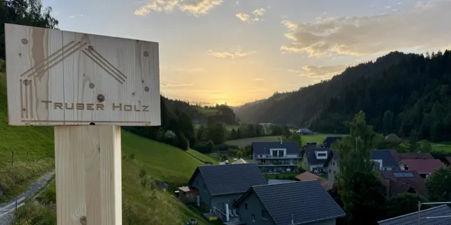 Zimmerleute montieren während der Aufrichtearbeiten eine vorgefertigte Holzkonstruktion auf einem Gebäude. Ein Kran hebt ein grosses Dachelement an seinen Platz, während mehrere Fachkräfte auf dem Dach die Montage begleiten.