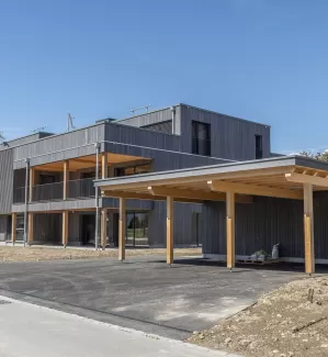 Mehrfamilienhaus Truberholzhaus Recherswil, Schweizer Holz, Truberholzwände sind nicht sichtbar, die Dübel sind nicht sichtbar, Fassade ist vorvergraut, es hat eine Attikawohnung, im Erdgeschoss und Obergeschoss hat es Loggaeinschnitte (Terrasse, Balkon), moderner Neubau, auf dem Dach ist ein Sonnensegel, Flachdach mit Solarpanel, es hat kein Keller dafür ein zusätzliches Gebäude mit Autounterstand und Lagerraum, Umschwung mit Rasen 