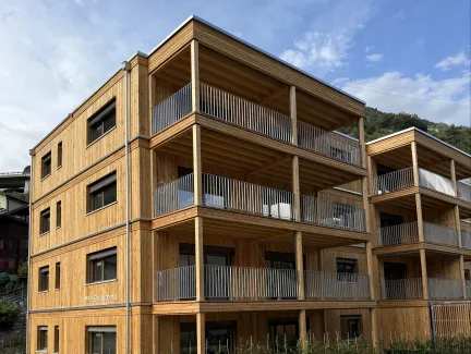 Mehrfamilienhaus in moderner Holzbauweise mit vier Geschossen, grosszügigen Balkonen und Holzfassade.