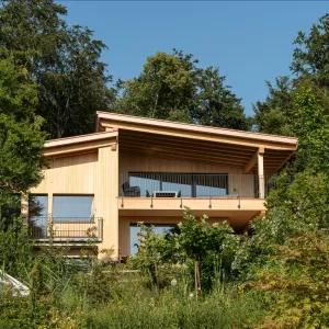 Truberholz Einfamilienhaus mit integrierter Arven-Täfer Wand. Schlafzimmer mit integrierter Dusche und Waschtisch. In der Dusche ist eine Brettstappel-Decke und der Boden ist aus ein Eschen Riemenboden. Die Wände sind Truberholz sichtbar. Die Decke ist leicht in der Dachschräge und ist eine Massivholzplatte. In der Wohnstube ist ein Cheminée mit Sitzoffen/Sitzbank.