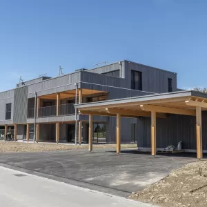 Mehrfamilienhaus Truberholzhaus Recherswil, Schweizer Holz, Truberholzwände sind nicht sichtbar, die Dübel sind nicht sichtbar, Fassade ist vorvergraut, es hat eine Attikawohnung, im Erdgeschoss und Obergeschoss hat es Loggaeinschnitte (Terrasse, Balkon), moderner Neubau, auf dem Dach ist ein Sonnensegel, Flachdach mit Solarpanel, es hat kein Keller dafür ein zusätzliches Gebäude mit Autounterstand und Lagerraum, Umschwung mit Rasen 