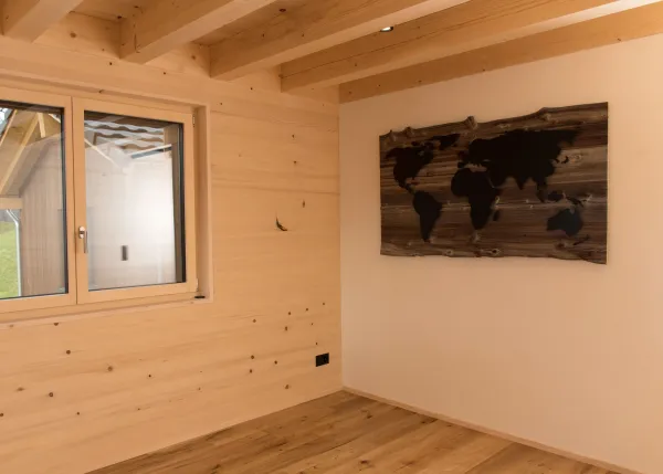 Innenansicht eines modernen Holzbaus mit sichtbaren Balken, natürlichen Holzoberflächen und massgefertigten Einbauten. Grosszügige Fensterflächen sorgen für viel Tageslicht und unterstreichen die warme, ruhige Wohnatmosphäre. Hochwertige Materialien und präzise Schreinerarbeiten prägen das Gesamtbild.
