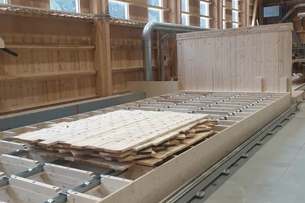 Produktionsstart Wandelemente Kunstpavillons   In unserer Produktionsstätte in Trub haben die Arbeiten zu den Wandelementen begonnen. Die Fertigungsanlage umfasst einen Produktionstisch, ein Dübelportal und ein Abbundportal. Die auf dem Produktionstisch ausgelegten Bretter werden vom Dübelportal vollautomatisch bei den Kreuzungspunkten verbunden. Das Abbundportal fräst die Konturen, bohrt die Steckdosen, kehlt die Verbindungsnuten und kalibriert die Elemente auf die gewünschte Dicke.