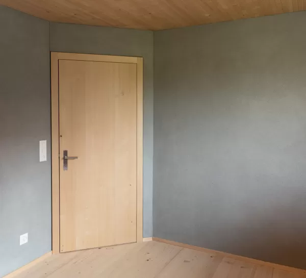 Truberholz Mehrfamilienhaus. Aussenschalung vor vergrautes Falzbrett aus Tanne, integrierte Sauna in Ferienwohnung, Saunawand aus Tanne, Möbel in der Saune aus Arven Holz, Truberholz-Wände innen sichtbar, inklusive Decke Dachschräge, Gebäudehülle Truberholz sichtbar, Innendecke Brettstapel, Boden ist alles Trockenbauaufbau, Zimmer und Bad aus Tannen Holz und allgemein Räume sind Buchenriemenboden. Türen sind alle Massivholz mit Blockfutter aus Tanne.